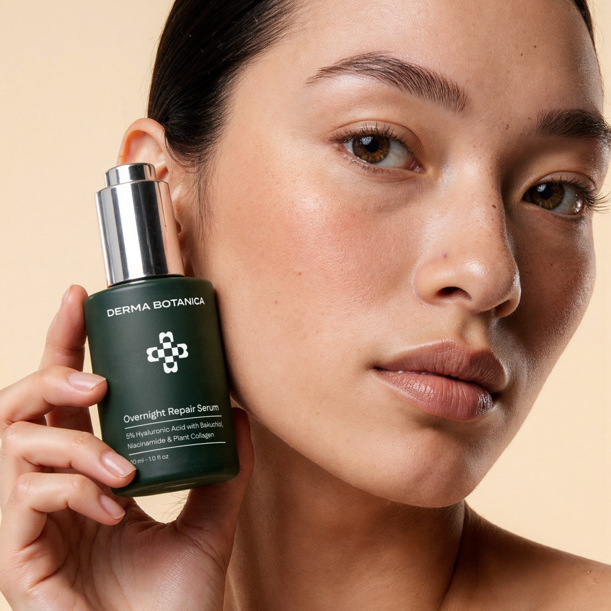 Woman holding a Derma Botanica Overnight Repair Serum bottle against a beige background